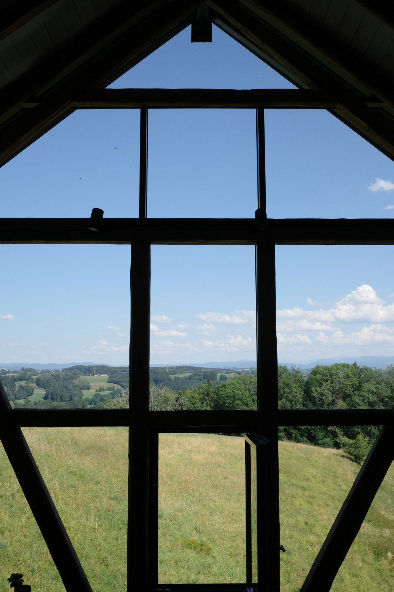 Blick durch ein gro&szlig;es Fenster auf gr&uuml;ne H&uuml;gel.